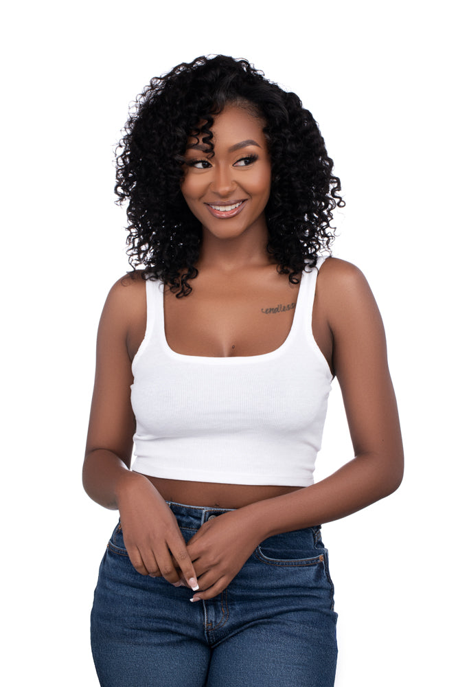 Woman with short curly wig wearing a white top and blue jeans on a white background