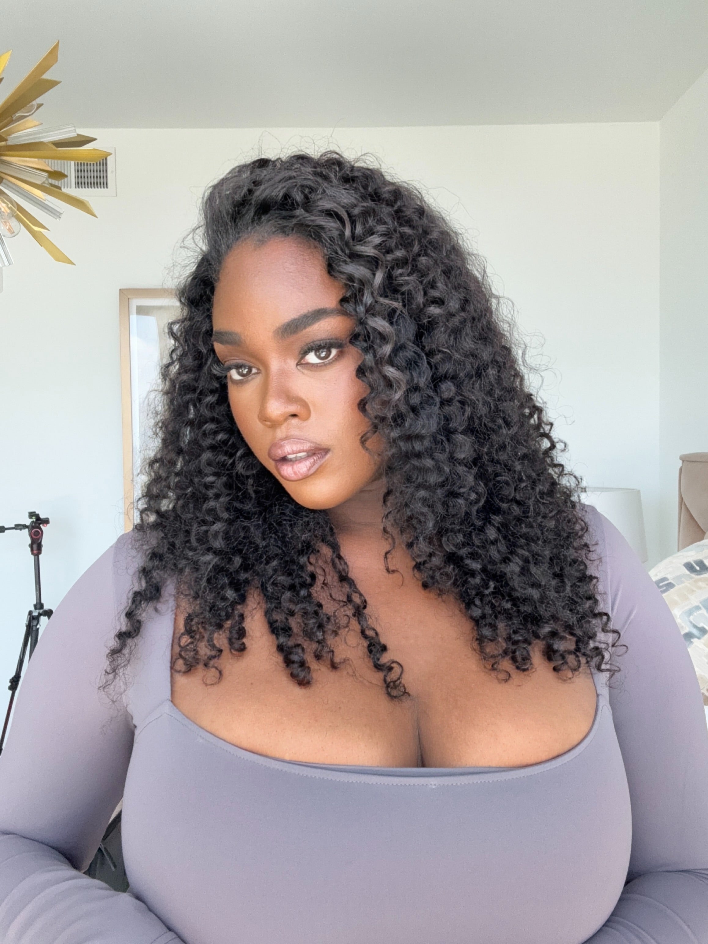 Woman with shoulder length curly wig wearing a white top and blue jeans on a white background