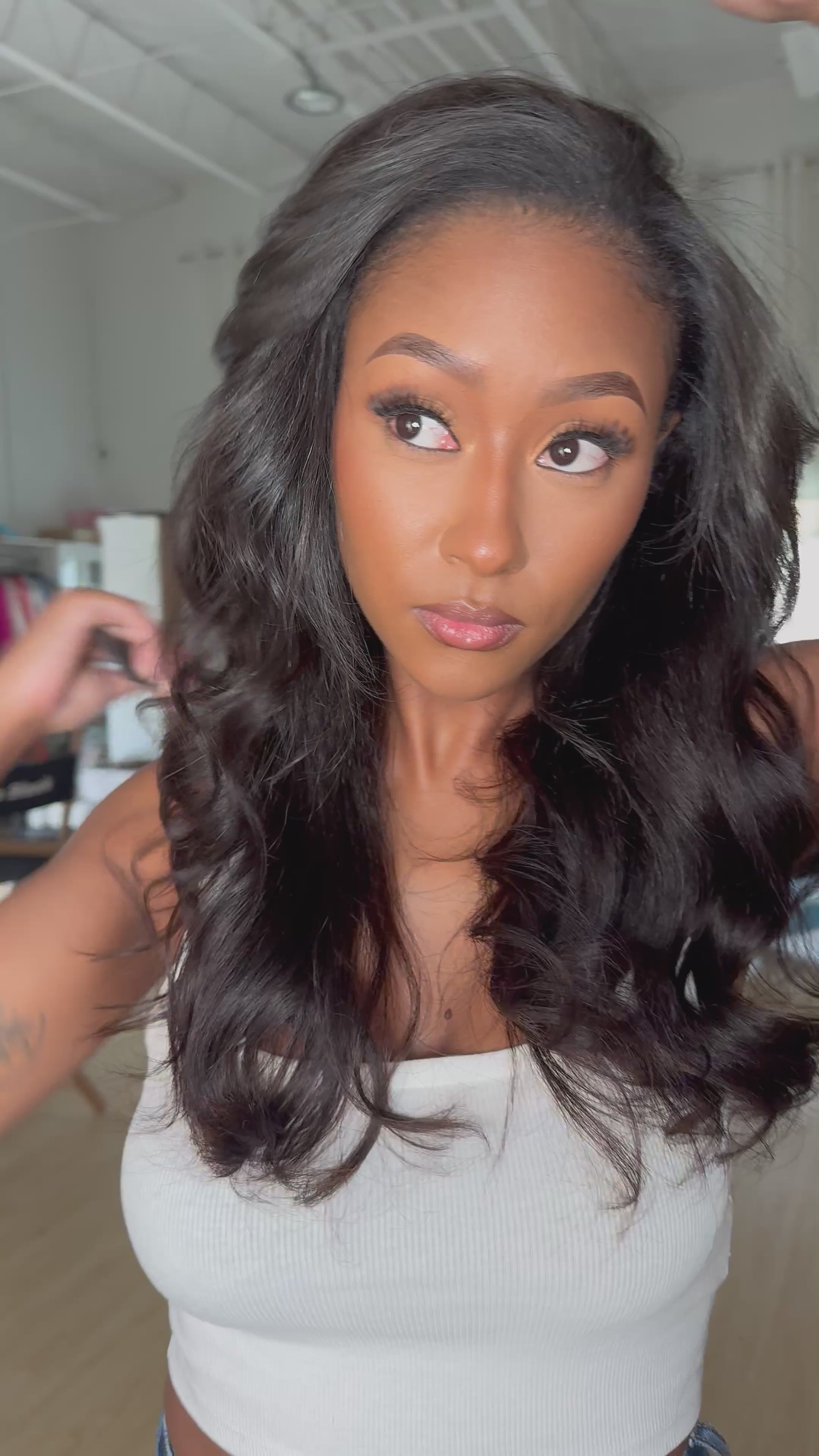  Black woman in white crop top gently fluffing her styled kinky straight clip-in hair extensions with soft curls