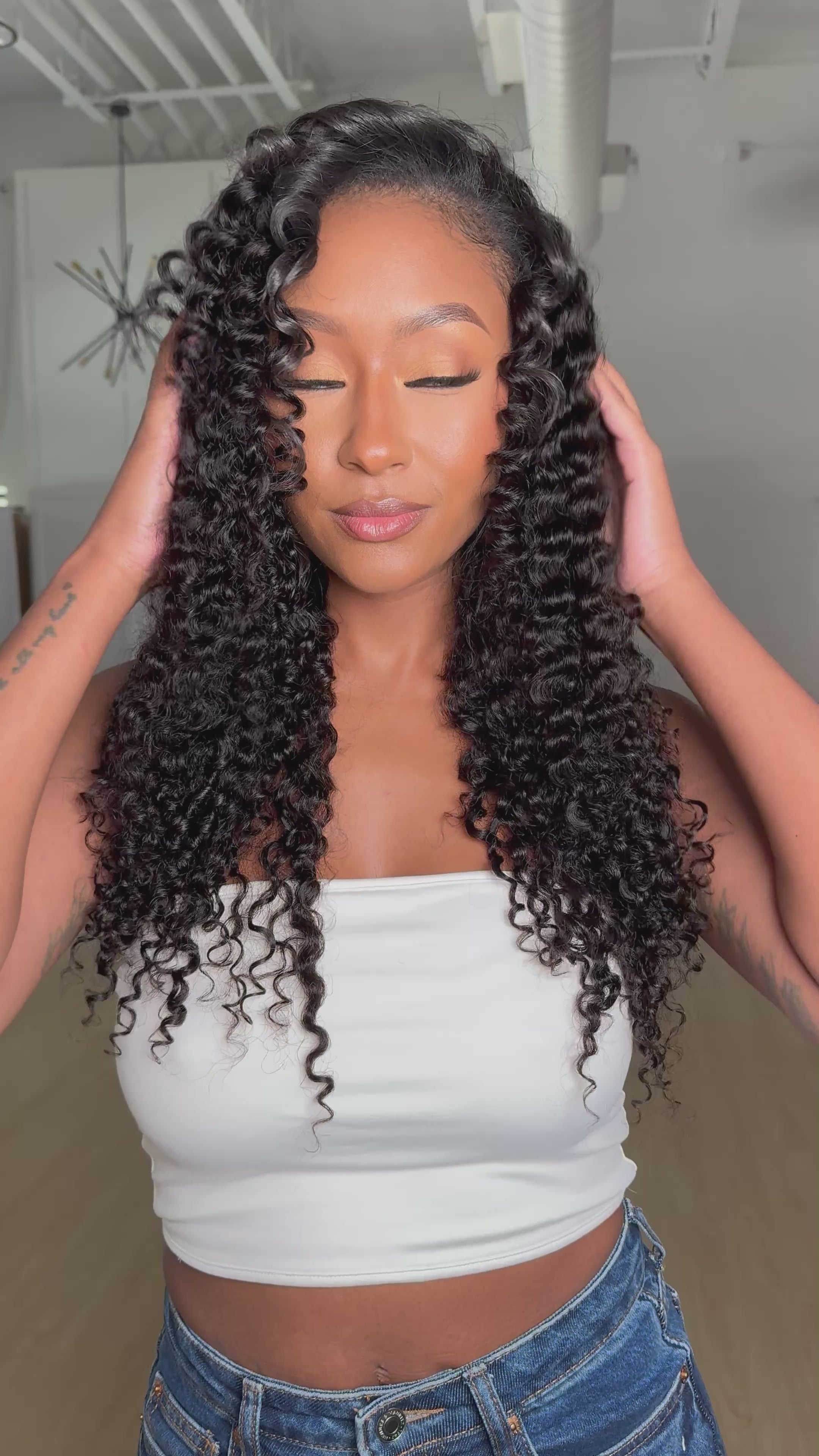 Woman with long curly wig wearing a white top and blue jeans on a white background