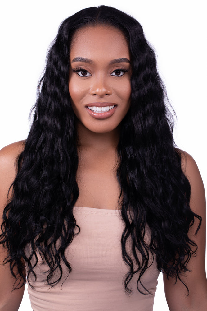 Confident woman with long Seamless Clip-Ins: “Venus” Body Wave, wavy black hair wearing a nude-colored strapless top, smiling at the camera against a white background.